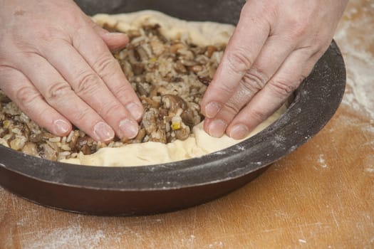 Making pie. Putting filling on raw dough in black metal baking form