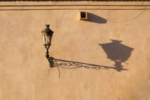 Old lantern on a dark yellow wall in the medina of Marrakesh. Long shadow during the golden hour.