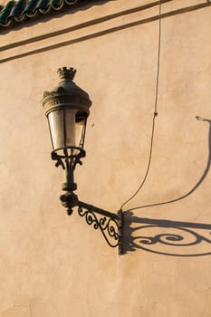 Old lantern on a dark yellow wall in the medina of Marrakesh. Long shadow during the golden hour.