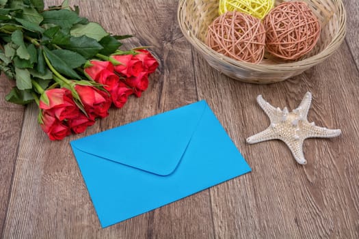 Blue envelope, red roses and white starfish on a wooden background