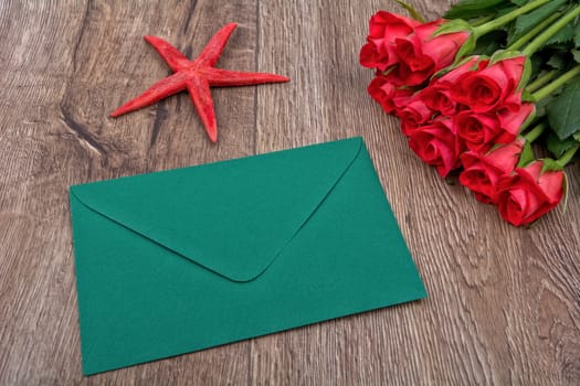 Green envelope, red roses and red starfish on a wooden background