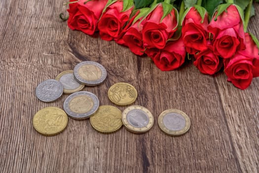 Euro coins and red roses on a wooden background