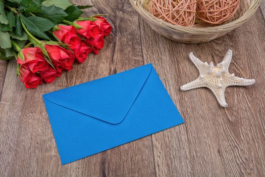 Blue envelope, starfish and red roses on a wooden background