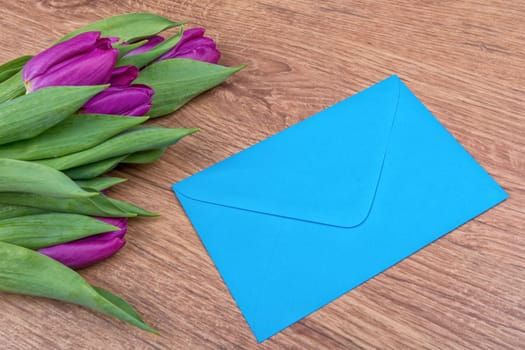 Blue envelope and violet tulips on a brown wooden background