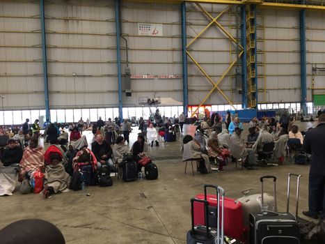 BELGIUM, Brussels: Passengers sit as they way inside a hangar at Zaventem airport on March 22, 2016, after terrorist bombings killed at least 30 people, both at the airport and at Maelbeek metro station.Pictures show hundreds of passengers stranded after the attack.