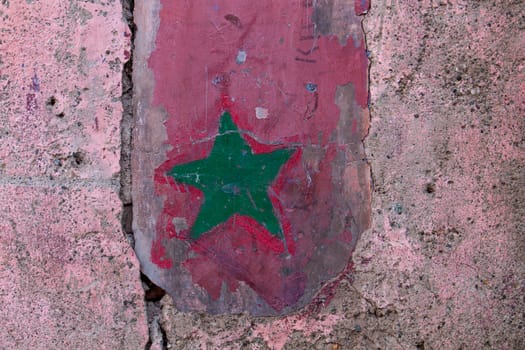 Old wall loosing its original color, with a sign of a moroccan flag, green star on the red background.