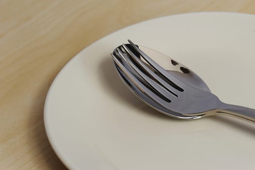 Fork and spoon on top of empty plate on wood table