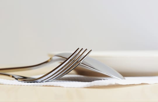 close up fork and spoon on white napkin with plate on back