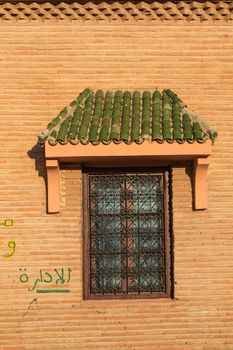 Closed window with an ornamental lattice and with a small roof with green tiles. Wall made of small bricks.
