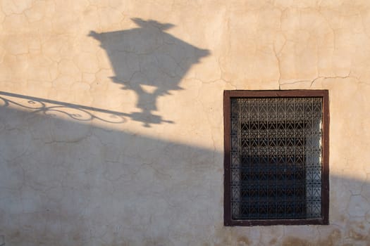 Old wall during the golden hour with a shadow of the old lantern and traditional window with lattice. Marrakesh, Morocco.