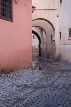 Dawn in the street of old medina of Marrakesh. Orange wall with traditional window, underpass with traditional arch. Puddles on the street after a night storm.