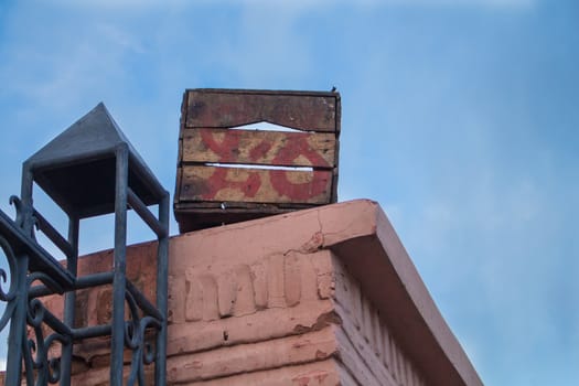 Orange decorated wall, part of a blue fence and a wooden old box on the wall. Blue sky during dawn with soft white clouds. Souk of Marrakesh, Morocco.