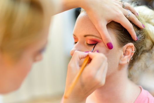 Make-up artist applying the eyeliner to model.