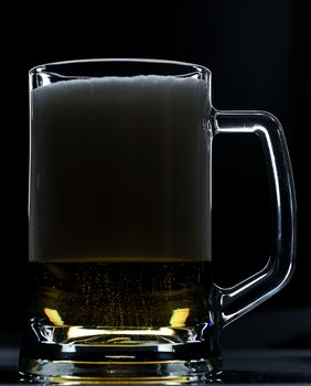 Glass with beer full of foam in half on black background