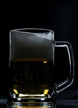 Glass brown beer with a lot foam on black background