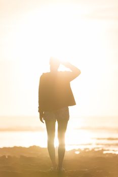 Silhouette of casualy dressed sporty woman watching sunset at the beach.