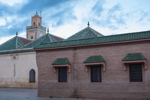 Streets still empty during dawn. Buildings and tower of the Ben Youssef Mosque in the medina of Marrakesh. Cloudy morning sky.