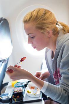 Woman eating meal on commercial airplane. 