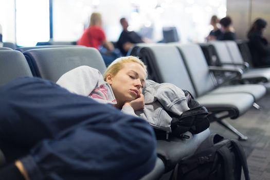 Tired female traveler sleeping on the airpot departure gates bench with all her luggage by her side.  Tireing travel concept.