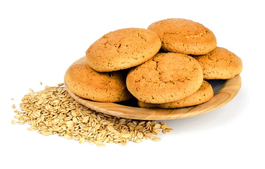 Two oatmeal cookies on a wooden plate and scattered oat flakes, isolated on white background.