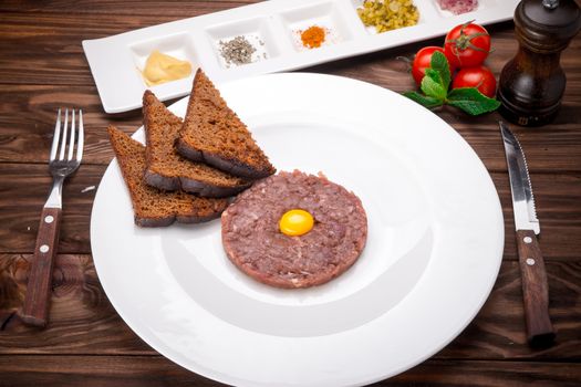 Beef tartare with spices and seasoning on wooden background