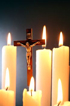 Small crucifix hanging on gray background among lighting candle