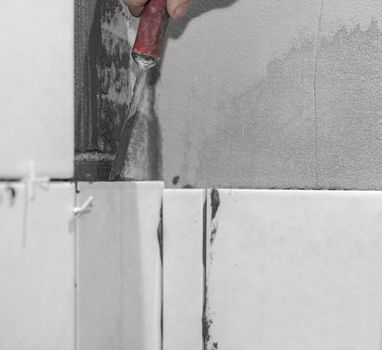 Worker tiler puts ceramic tiles on a wall