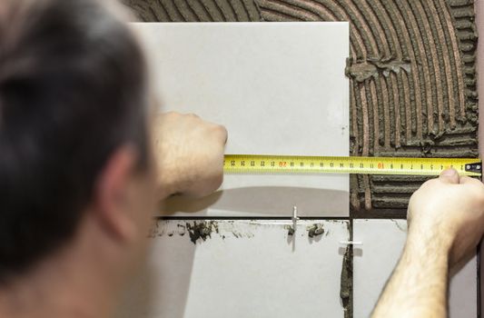 Worker tiler puts ceramic tiles on a wall