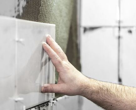 Worker tiler puts ceramic tiles on a wall
