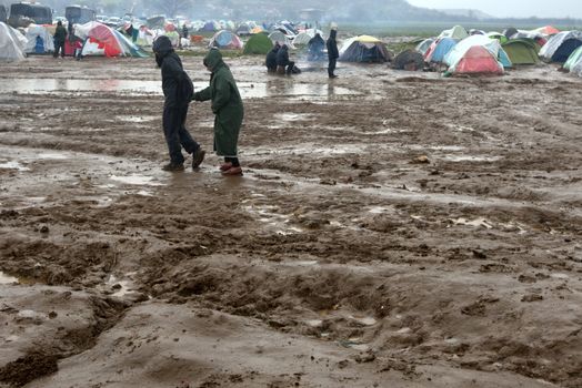 GREECE, Idomeni: Two people walk in mud as thousands of migrants are stranded in a makeshift camp for migrants and refugees at the Greek-Macedonian border near the village of Idomeni on March 23, 2016. The UN refugee agency harshly criticized an EU-Turkey deal on curbing the influx of migrants to Greece, saying reception centers had become detention facilities, and suspended some activities in the country. The EU and Ankara struck a deal aiming to cut off the sea crossing from Turkey to the Greek islands that enabled 850,000 people to pour into Europe last year, many of them fleeing the brutal war in Syria.