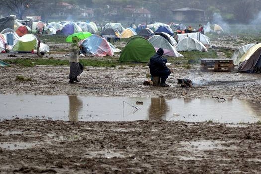 GREECE, Idomeni: One person walks in mud as thousands of migrants are stranded in a makeshift camp for migrants and refugees at the Greek-Macedonian border near the village of Idomeni on March 23, 2016. The UN refugee agency harshly criticized an EU-Turkey deal on curbing the influx of migrants to Greece, saying reception centers had become detention facilities, and suspended some activities in the country. The EU and Ankara struck a deal aiming to cut off the sea crossing from Turkey to the Greek islands that enabled 850,000 people to pour into Europe last year, many of them fleeing the brutal war in Syria.