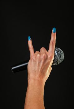 Woman hand with blue nails holding microphone with devil horns rock metal sign isolated on black background