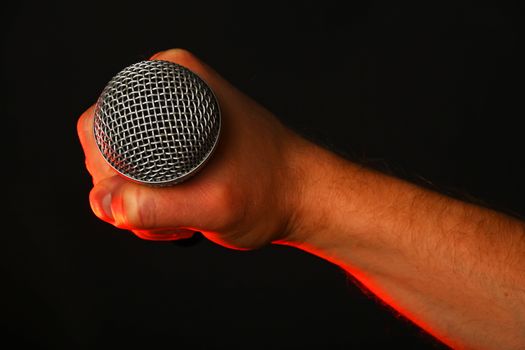 Male hand holding microphone highlighted with red gun projector isolated on black background