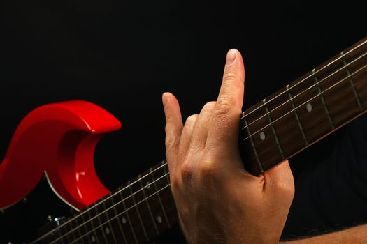 Male hand holding red sg guitar neck with devil horns rock metal sign isolated on black background