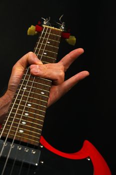 Male hand holding red sg guitar neck with devil horns rock metal sign isolated on black background