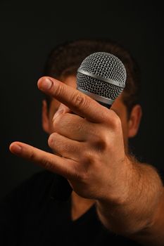 Male hand holding microphone with devil horns rock metal sign with head behind isolated on black background