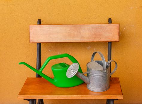 a corner of the terrace with  a wooden bench and a watering-can of aluminium  and a plastic one