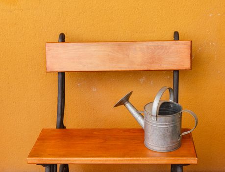 a corner of the terrace with  a wooden bench and a watering-can of aluminium