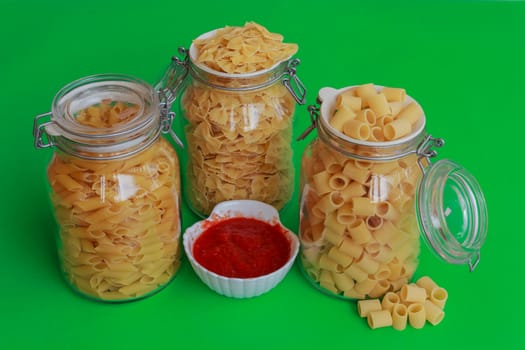 different sizes of pasta to choose from confined in glass jars with bowl of red sauce