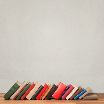 Old colorful leaning books on wooden floor near the white wall