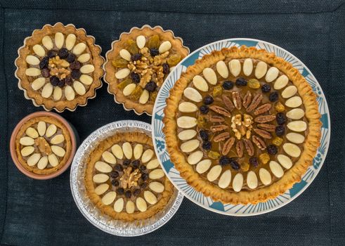 Five round traditional Polish Easter cakes "Mazurek" with almonds, raisins and walnuts on the dark fabric background.