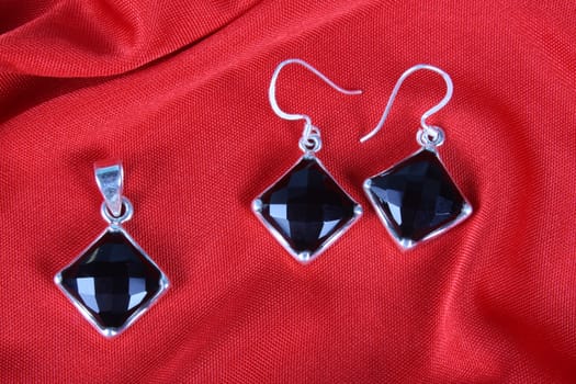 A set of black onyx jewelery made in silver consisting of a pendant and a pair of earrings, on red fabric.