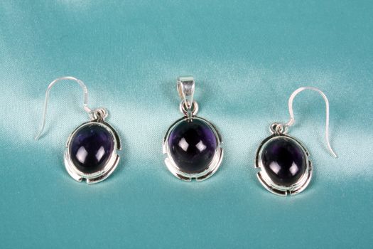 A jewelery set of semi precious purple gemstones in silver pendant and earrings.