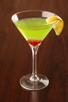 Green apple martini with a wedge of lemon and a maraschino cherry.