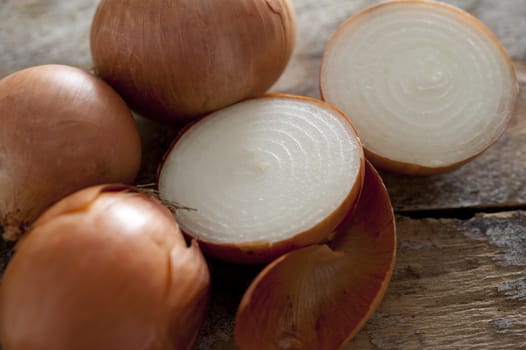 Close up of three whole and one halved fresh spanish onion with papery skin on a rustic wooden surface