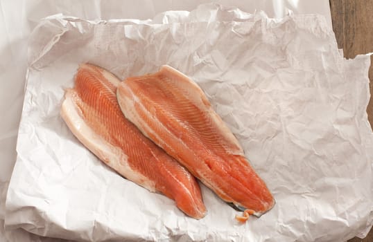 High angle view of two pink uncooked fish fillets displayed on white wrinkled paper