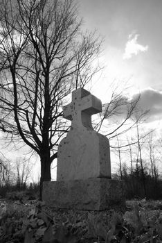 An old tombstone in a quiet gravesite with the sunshine backlighting the cross in a spirtual manner.