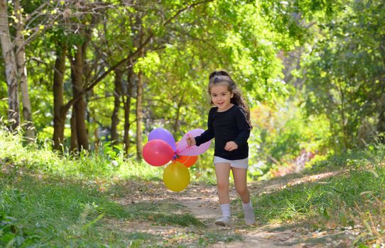 Little girl playing in autumn park with balloons