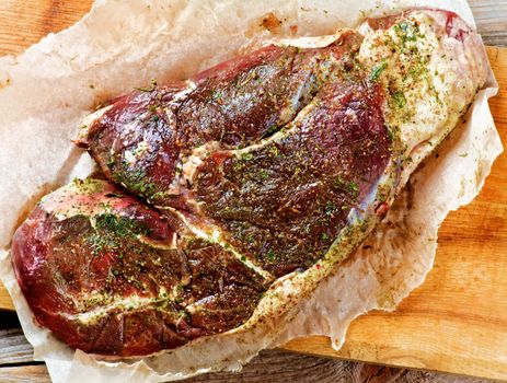 Perfect Raw Beef Shoulder Marinated with Spices and Herbs on Parchment Paper closeup on Wooden Cutting Board. Top View