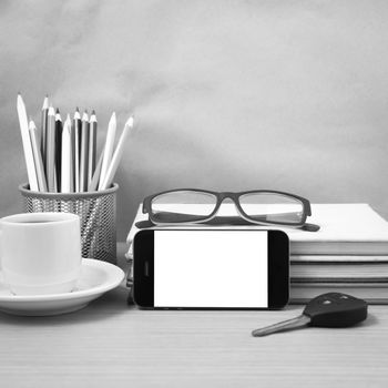 office desk : coffee and phone with car key,eyeglasses,stack of book,pencil box black and white color